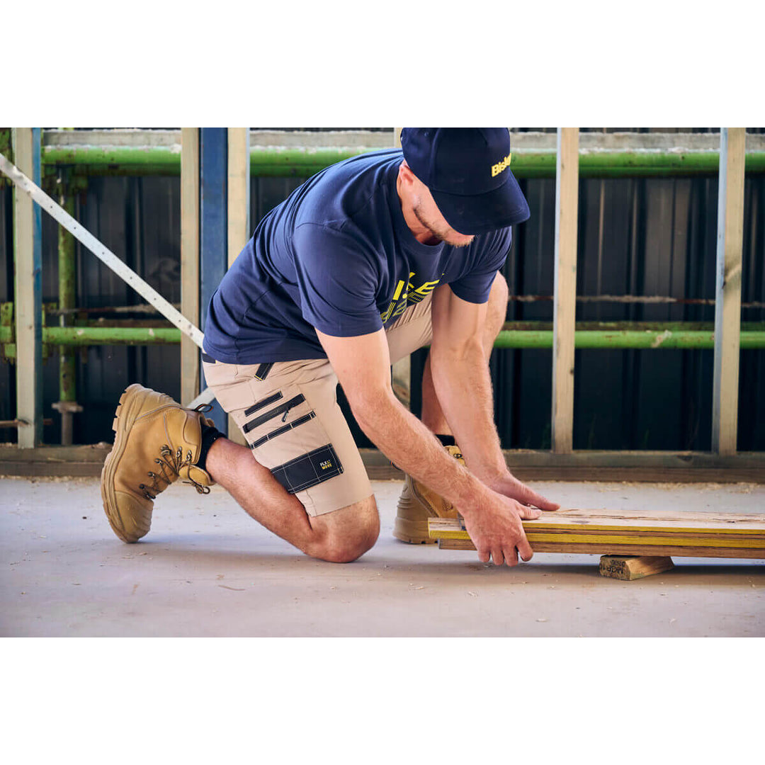 Person in work attire, wearing a Bisley BCAP50 Cap, kneeling on a concrete surface with tools.
