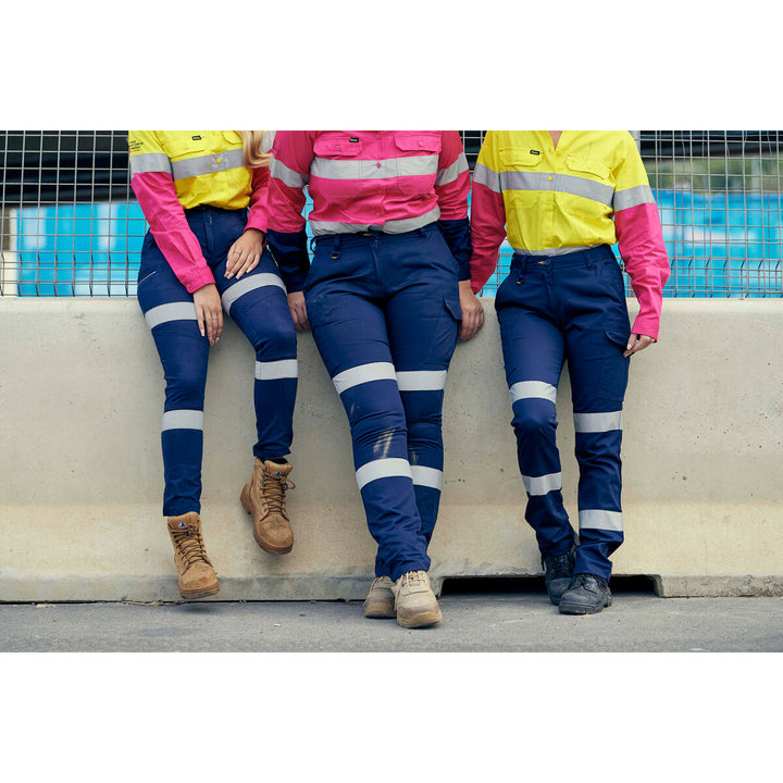 Three women wearing Bisley BL6896 high-visibility workwear sitting on a concrete ledge.